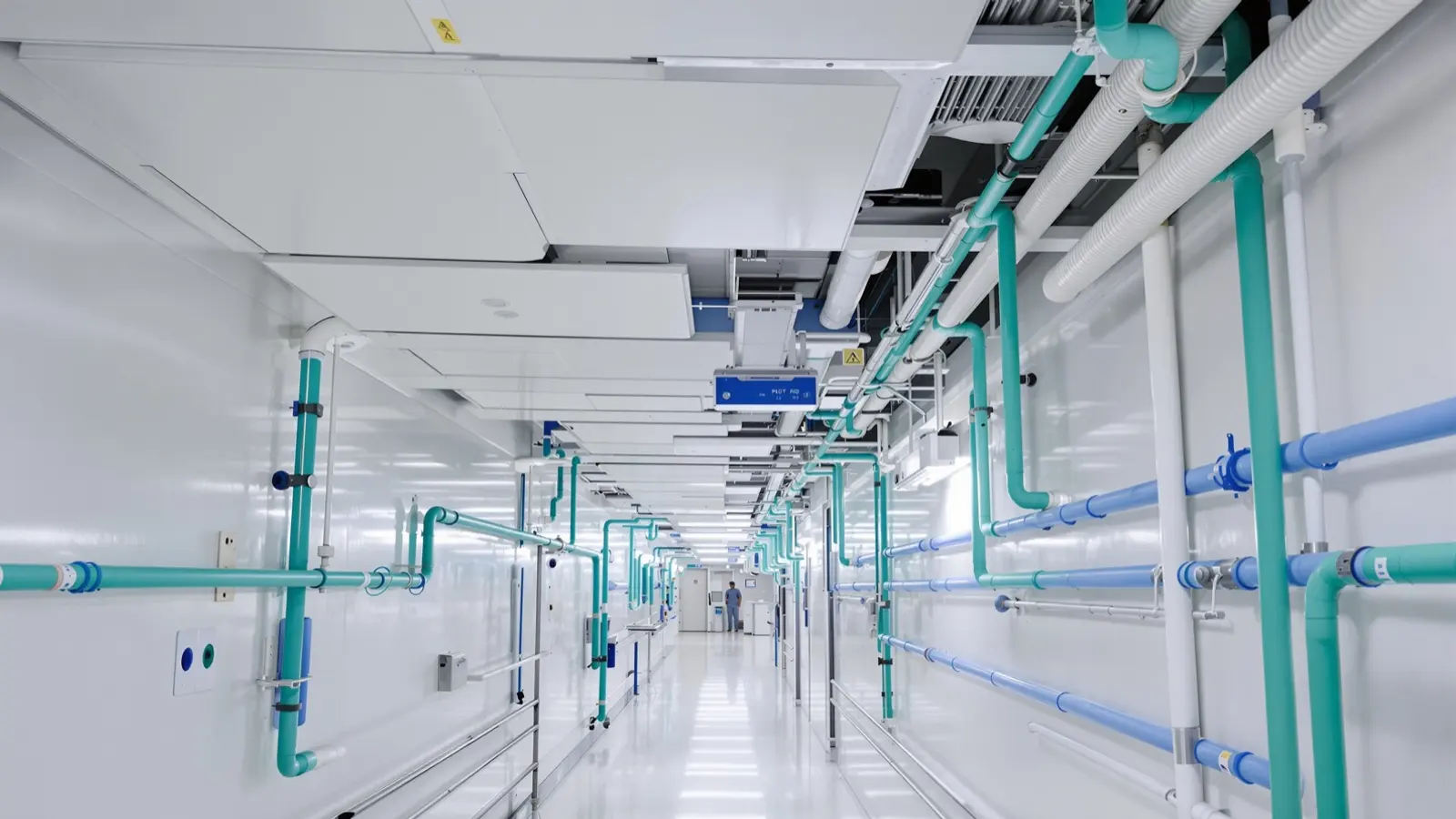 Pasillo técnico de hospital con el plafón abierto, ductos de aire y tuberías de gases medicinales en verde y azul a lo largo del muro